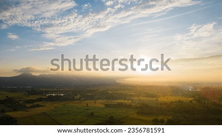 Aerial view of a bright yellow morning sunrise above dense white clouds with a blue sky overhead.