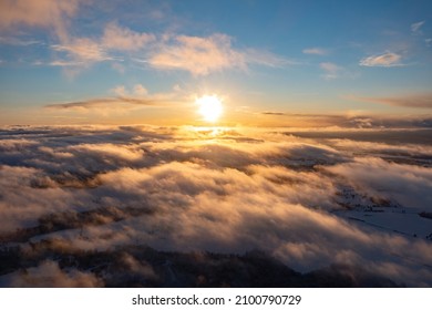 Aerial view of bright yellow sunset over white dense clouds with blue sky overhead. - Shutterstock ID 2100790729