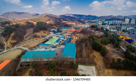 Aerial View Of Buildings And Cars In Small Rural Industrial Park Under Cloudy Skies.