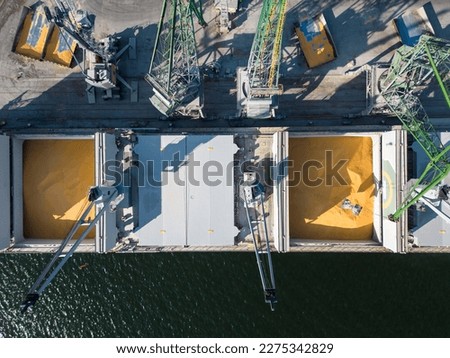 Aerial view of a bulk carrier ship loaded with grain is docked at a busy port, with workers and machinery seen in the background.