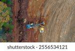 An aerial view of a bustling construction site shows bulldozers, trucks, and grading equipment shaping the land, with dirt roads, cleared areas, and scattered materials.



