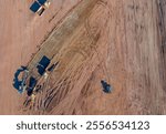 An aerial view of a bustling construction site shows bulldozers, trucks, and grading equipment shaping the land, with dirt roads, cleared areas, and scattered materials.



