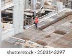 Aerial view of busy industrial under construction site workers working with cranes and excavators. Top view of precast concrete slap floor full of steel. Development high rise architecture building.