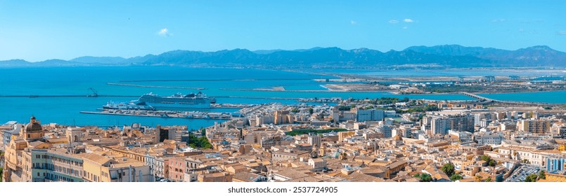 Aerial view of Cagliari, Sardinia, featuring historical and modern architecture, a docked cruise ship, and the Mediterranean Sea with rugged mountains. - Powered by Shutterstock