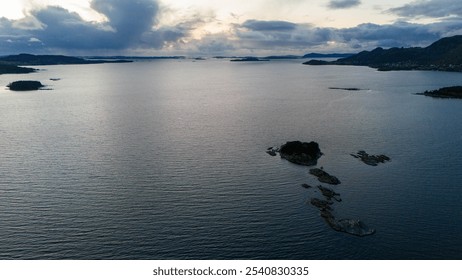 Aerial view of a calm fjord with small rocky islands and distant mountains under a cloudy sky. - Powered by Shutterstock