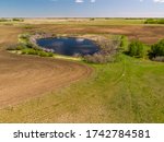 An aerial view of a calm secluded peaceful pond surrounded by trees and other natural growth in the wide open prairies of Saskatchewan, Canada. 