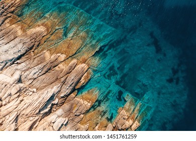 Aerial view of calm turquoise sea water and rocks from molten lava from drone. Pattern of sea surface and rocky shore. Thracian Sea, Greece. Rocky coast of the peninsula