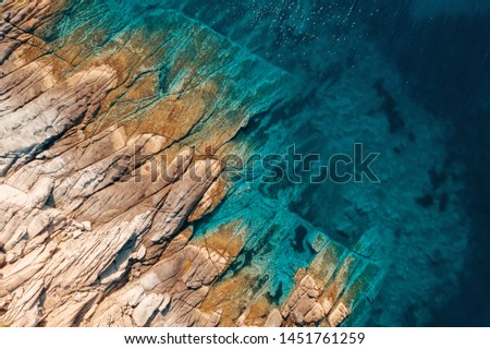 Aerial view of calm turquoise sea water and rocks from molten lava from drone. Pattern of sea surface and rocky shore. Thracian Sea, Greece. Rocky coast of the peninsula