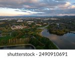 Aerial view of Canberra with lush greenery, residential buildings, and a tranquil lake under a partly cloudy sky at sunset.