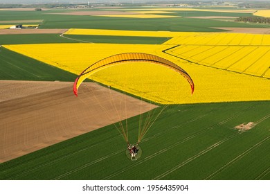 Vue aérienne du canola: paramoteur en gros plan survolant les champs de colza jaune avec soleil printanier. Département de l'Essonne, France