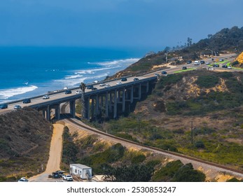 An aerial view captures a coastal highway bridge in San Diego, California, with the Pacific Ocean on the left and a railway track below, amidst rolling hills. - Powered by Shutterstock