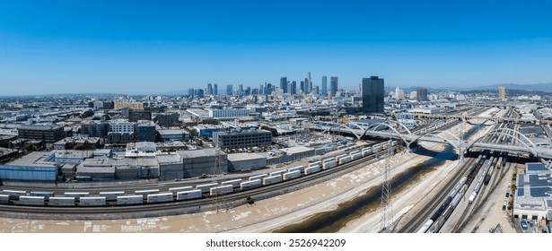 An aerial view captures downtown Los Angeles with the skyline, Los Angeles River, train tracks, and the Sixth Street Viaduct under a clear blue sky. - Powered by Shutterstock