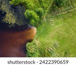 An aerial view captures the gentle confluence of a tawny river with the surrounding verdant landscape, a natural tapestry of earthy hues and vibrant greens.