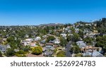 An aerial view captures a Los Angeles neighborhood with diverse homes and lush greenery, set against the backdrop of the iconic Hollywood Sign and clear blue sky.