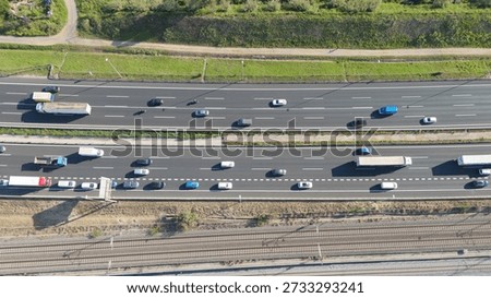 Aerial view capturing a busy multi-lane highway with traffic flowing. Featuring cars. Trucks. And a motorcyclist traveling in both directions parallel to railway tracks. Infrastructure