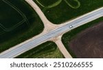 Aerial view of car driving on rural road intersection. Aerial shot of a car driving through a rural road intersection surrounded by green fields and farmland.
Latvia, spring