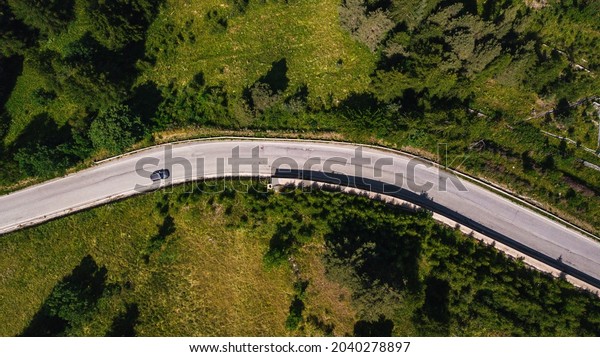 Aerial view of car on the move\
on road amidst lush green forest. Car passing on road through\
beautiful green forest cover. Top view of driveway along the\
forest