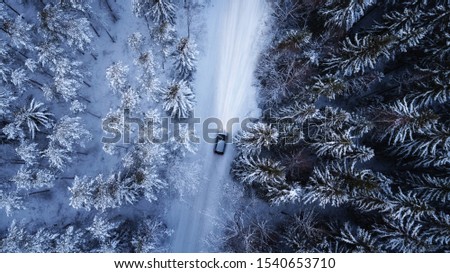 Aerial view of a car on winter road in the forest. Aerial photography of snowy forest with car on the road. Aerial photo. 