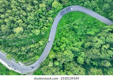 Aerial view car and truck driving on winding road through green forest. Sustainable transport. Electric vehicles and hydrogen energy trucks in natural landscape. Eco-friendly highway. Green logistics.