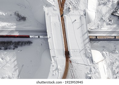 Aerial View Of Cargo Train Wagons Passing Under The Overpass, A Double-track Railway. Winter Rail Road With White Snow, Top View. Transport Infrastructure, Train Track, Snowy Landscape