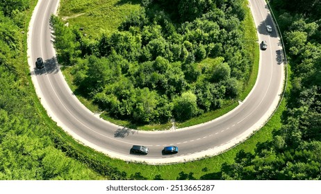 Aerial View of Cars Driving on Curved Road Through Forest. An aerial view of cars driving along a curved road cutting through a lush green forest. - Powered by Shutterstock