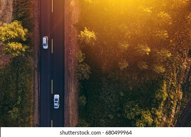 Aerial view of cars on the road through countryside in sunset, drone point of view