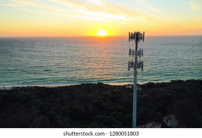 Aerial View Of A Cell Phone Tower (mobile Phone Tower) At Sunset, With The Orange Sun Setting Above A Blue Ocean And Clouds In The Sky