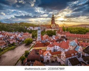 Aerial view of Cesky Krumlov along the Vltava river with St Jost church, medieval castle and houses with red roof, stunning colordful dramatic sunset sky