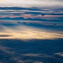 Aerial View Of A Cloudscape At Dusk, Showcasing Layers Of Clouds With The Setting Sun Casting A Soft Glow, Illuminating The Edges And Creating Shadows.