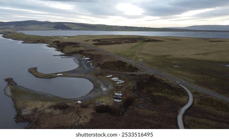 An aerial view of a coastal landscape with boats, a winding road, and a boardwalk, under a cloudy sky. - Powered by Shutterstock