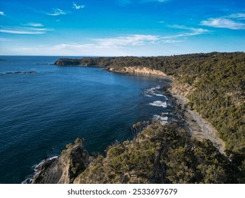 Aerial view of a coastal landscape with clear blue water and lush green forested cliffs. - Powered by Shutterstock