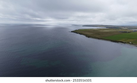 Aerial view of a coastal landscape with a cloudy sky, green fields, and calm sea waters. - Powered by Shutterstock