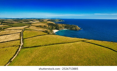 Aerial view of a coastal landscape featuring lush green fields, a serene blue sea, and a small sandy beach nestled in a cove. In Cornwall, UK. - Powered by Shutterstock