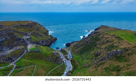 Aerial view of a coastal landscape featuring rugged cliffs, a winding road, and the ocean in the background. In Tintagel, Cornwall, UK. - Powered by Shutterstock