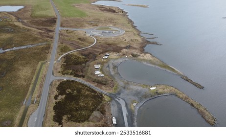 Aerial view of a coastal landscape with winding roads, parked cars, and boats near the water. - Powered by Shutterstock