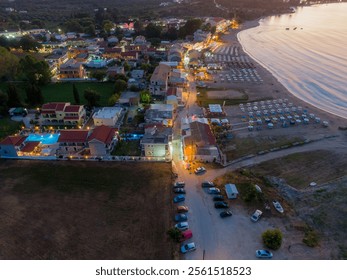 Aerial view of coastal town at dusk, with illuminated buildings, beach umbrellas, and parked cars. - Powered by Shutterstock