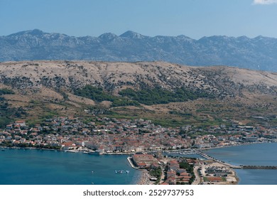 Aerial view of a coastal town with mountain backdrop, red-roofed buildings, and a vibrant seaside beach. Summer day in a Mediterranean coastal town surrounded by rugged hills and clear blue waters. - Powered by Shutterstock