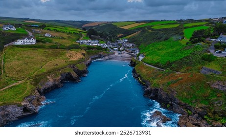 Aerial view of a coastal village surrounded by lush green hills and rocky shores. In Cornwall, UK. - Powered by Shutterstock