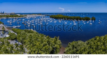 Aerial view of Coconut Grove Sailing Club at Dinner Key Marina in Miami, Florida. There are trees below at the shore and views of boats at the marina against the blue sky.
