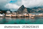 An aerial view of colorful wooden houses on stilts in a picturesque village in the Lofoten Islands, Norway, with majestic mountains in the background. Sakrisoy, Lofoten, Norway