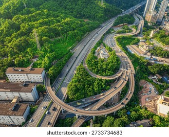 Aerial view of a complex highway interchange with curved ramps surrounded by lush green forest in a modern city during the day.