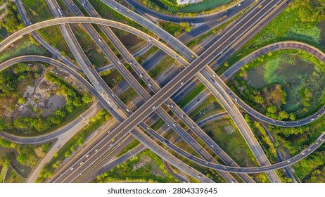 Aerial view of complex highway interchange with moving traffic surrounded by green trees in urban area captured in daylight