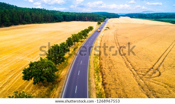 Aerial view of a country\
road with moving cars and trucks between agricultural fields in\
Europe, Germany. Beautiful landscape.  Captured from above with a\
drone