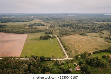 Aerial view of a countryside landscape with open fields, patches of forest, and winding rural roads under a cloudy sky. - Powered by Shutterstock