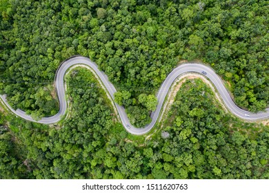 Aerial view of countryside road passing through the green forrest and mountain.