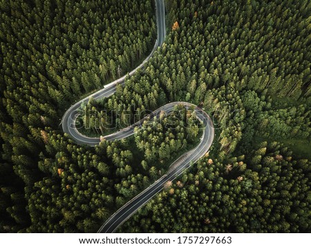 Aerial view of countryside road passing through the green forest and mountain