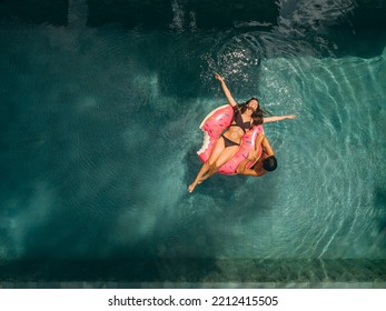 Aerial View Of Couple Having Fun In Resort Pool. Woman Lying On Donut Floatie Ring And Man In Water Next To Her.