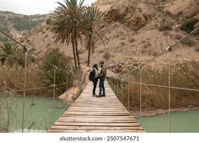 Aerial view of a couple walking in the beautiful wooden suspension bridge that crosses the Segura River in the charming town of Ojos in Murcia - Powered by Shutterstock