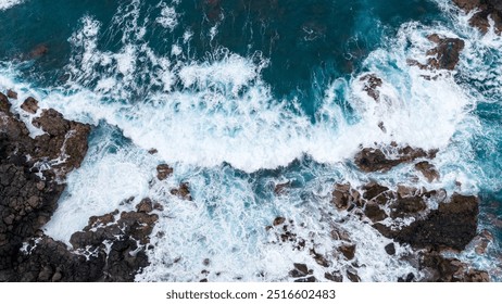 Aerial view of crashing ocean waves against rugged coastal rocks, displaying the dynamic beauty of turbulent sea foam and rocky shoreline. - Powered by Shutterstock