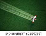 An aerial view of a crop duster or aerial applicator, flying low, and spraying agricultural chemicals, over lush green potato fields in Idaho.